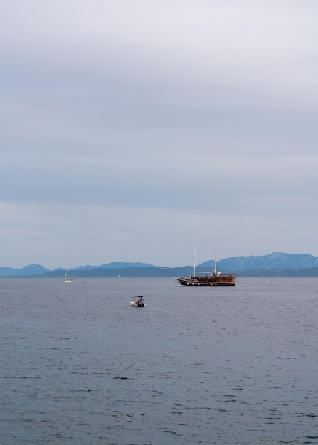 An old wooden boat with many tourists on board in the Adriatic Sea It's evening High mountains on the horizon Small yachts and boats sail nearby Croatia