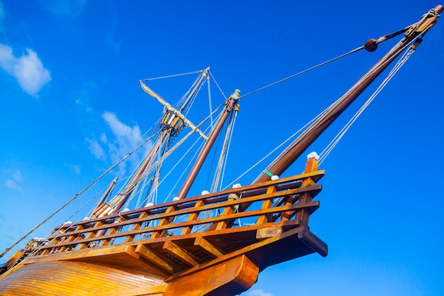 An old wooden caravel ship with folded sails against a blue sky with white clouds