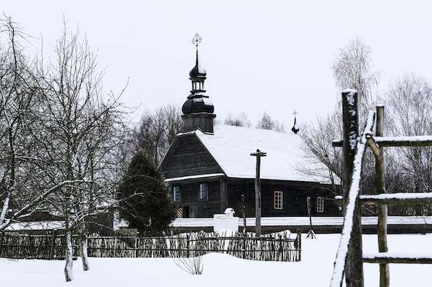 Old wooden church made of round logs Cross on the dome Winter Russian landscape Snow covered trees Abandoned old Russian village covered with snow