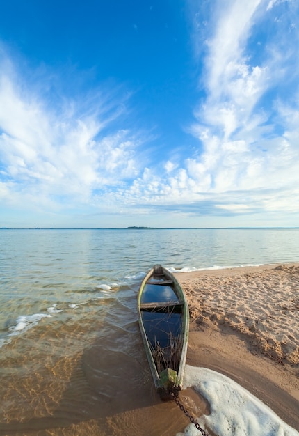 Old wooden fishing boat flooding near the lake shore and summer sky behind (Svityaz, Ukraine)