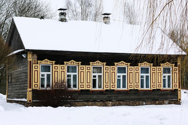 Old wooden house made of gray logs With beautiful yellow windows and shutters Winter Russian landscape Snow covered trees Abandoned old Russian village covered in snow