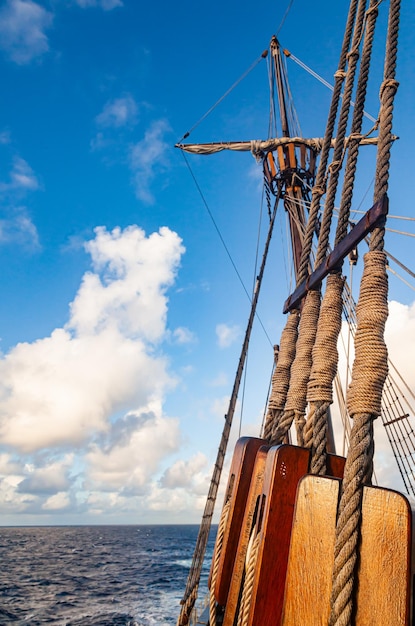 Old wooden sailing ship at sea with viewing basket on a wooden mast on tight ropes and a rope ladder