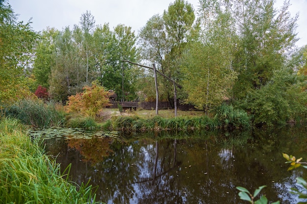 Old wooden well. Autumn Park. Trees reflected in the water of the lake in the park