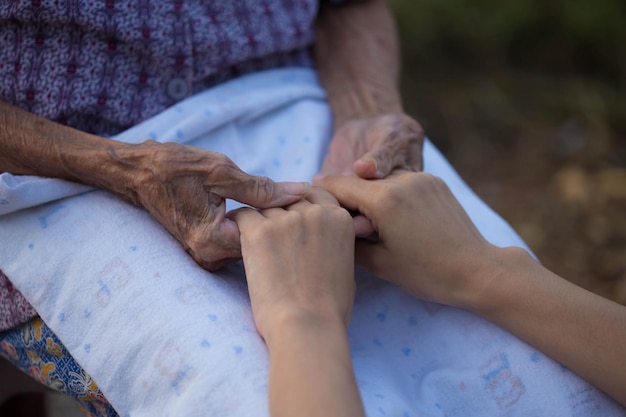 Old and young holding hands on light background closeup