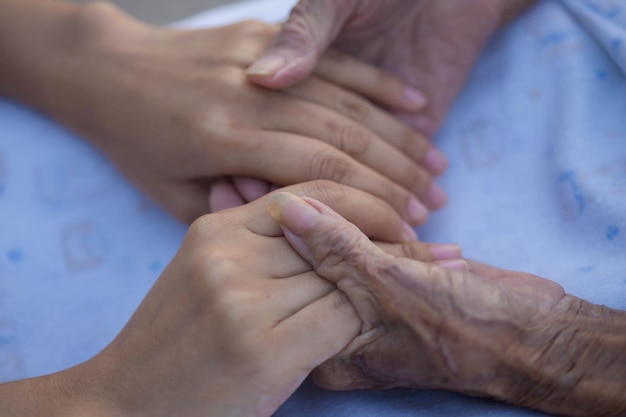 Old and young holding hands on light background closeup