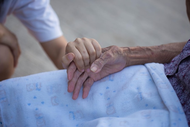 Old and young holding hands on light background closeup