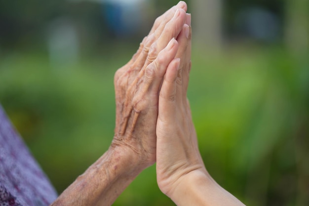 Old and young holding hands on light background closeup