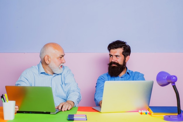 Old and young men looking at laptop screen watching movie or news in social network Two business peo