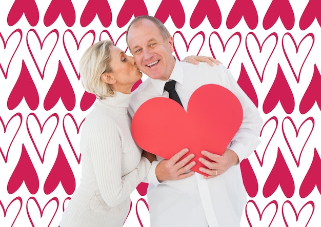 Older affectionate couple holding red heart shape against valentines day pattern