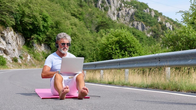 An older grayhaired man is working on a laptop