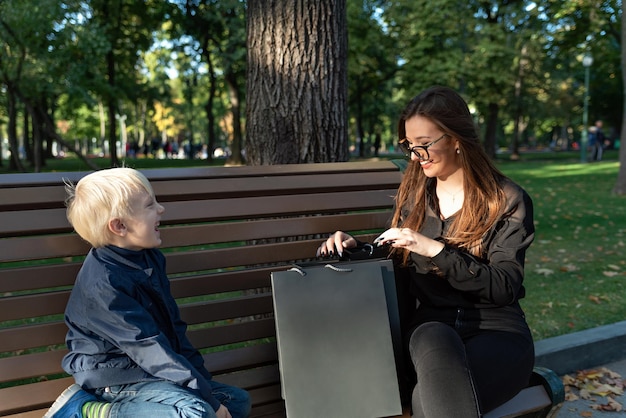 Older sister and her brother are sitting on bench in park and chat Happy family