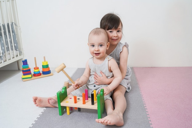 The older sister is playing with her younger sister. Girls play with a wooden toy.