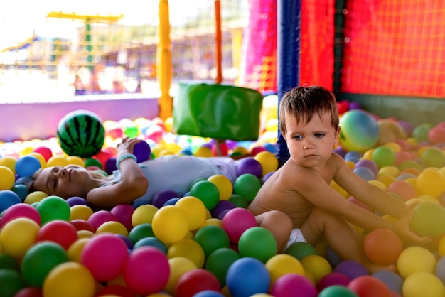 The older sister plays with her younger brother and throws small balls at him while sitting in the playroom