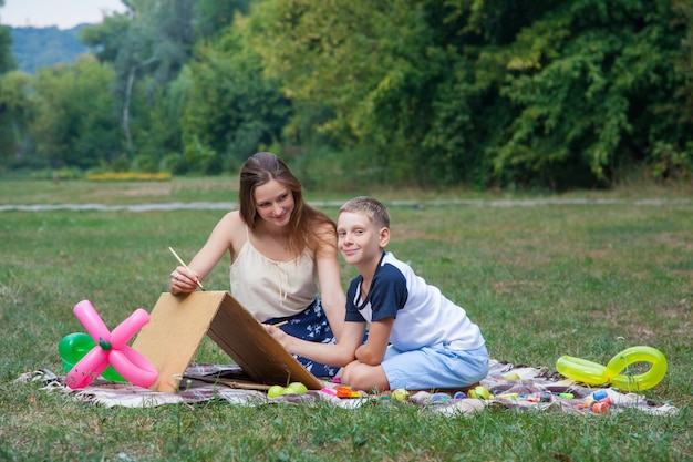 Older sister trying to teach her brother to paint in the park