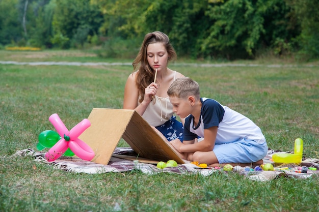 Older sister trying to teach her brother to paint in the park