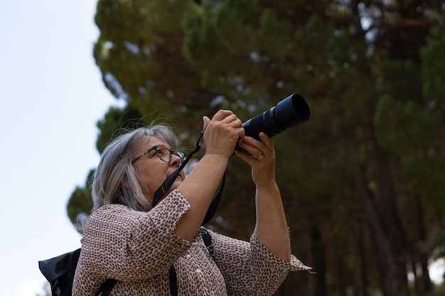 older white-haired woman taking pictures in the forest