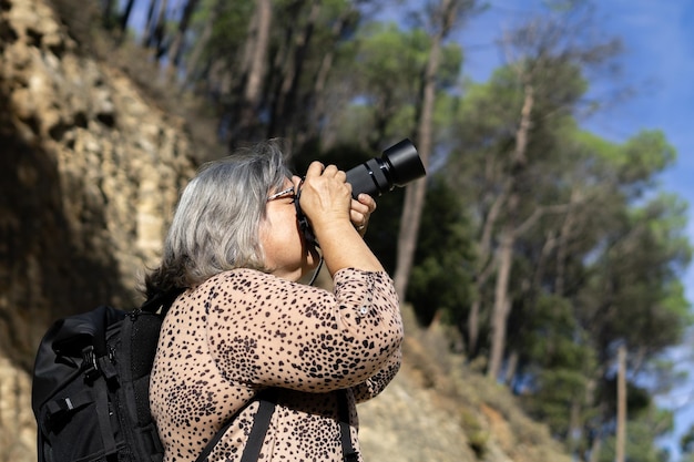 older white-haired woman taking pictures in the forest