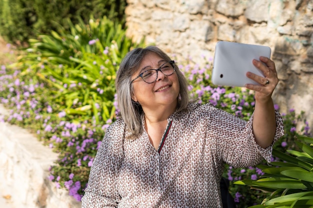 older white-haired woman with glasses looking at tablet in park