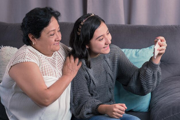 Older woman 60 year old latin grandmother using cell phone and having fun with her granddaughter