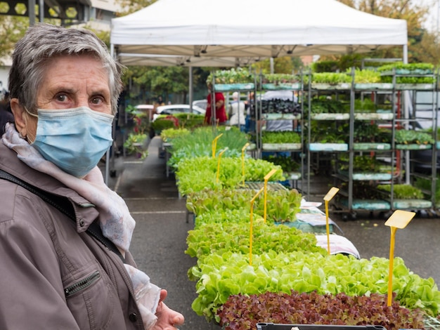 Older woman buying vegetables at a market, wearing a mask against the covid pandemic. Market concept