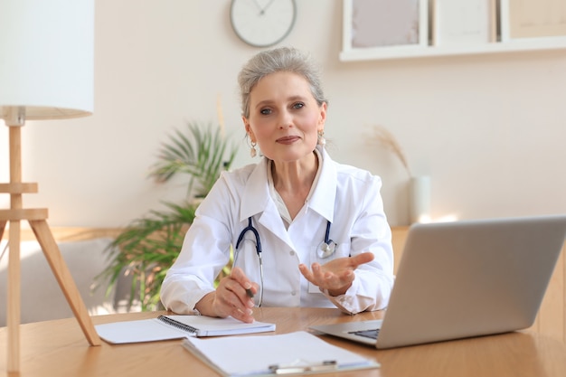 Older woman doctor therapist wearing headset video call talking to web camera consulting virtual patient online by video conference call chat.