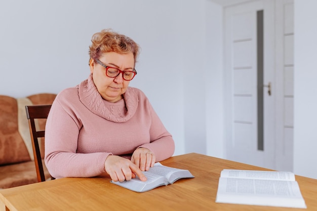 An older woman at home glasses perched on her nose sits comfortably in her favorite chair reading a