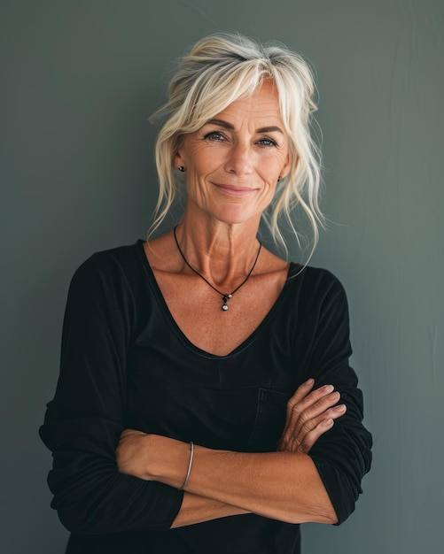 An older woman with her arms crossed standing in front of a gray wall