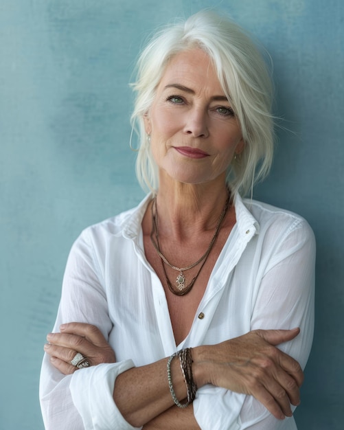 An older woman with white hair standing against a blue wall