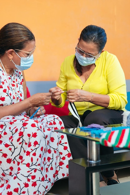 Older women with protective mask knitting at home