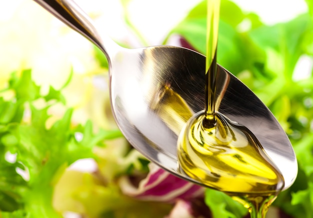 Olive oil being poured into a spoon over salad