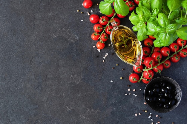 Olive oil in a glass sauceboat cherry tomatoes and basil on black background top view