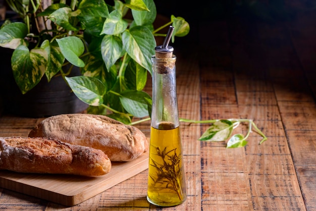 Olive oil with rosemary in a glass bottle on wooden table with buns