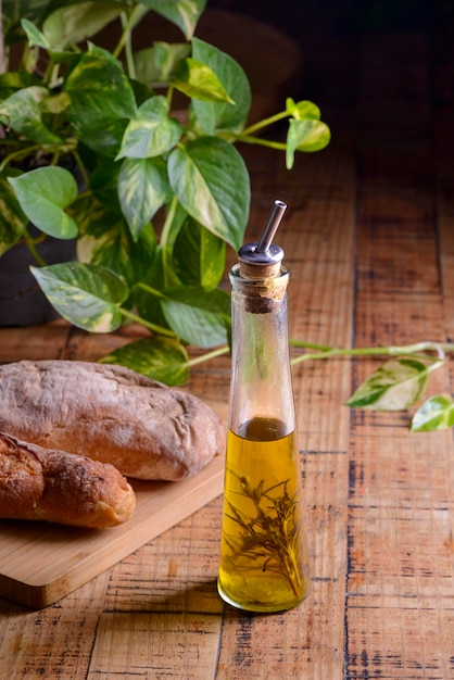 Olive oil with rosemary in a glass bottle on wooden table with buns