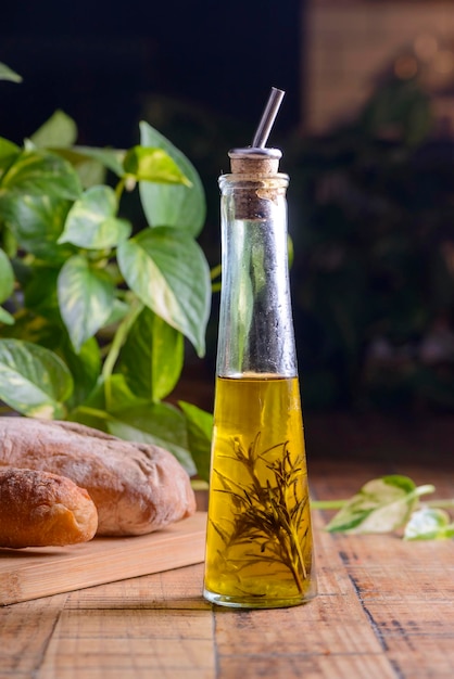 Olive oil with rosemary in a glass bottle on wooden table with buns