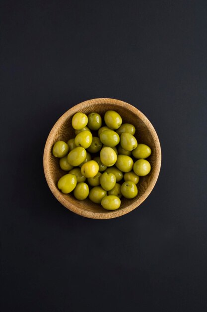 Olive in the wooden bowl on the black background Top view Closeup