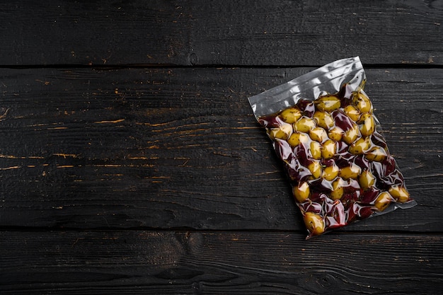 Olives in vacuum packaging for supermarket set, on black wooden table background, top view flat lay, with copy space for text