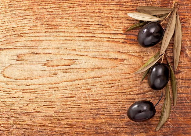 Olives over Wooden Background Dark olives with leaves on wooden background old wooden table olive branch background top view flat lay