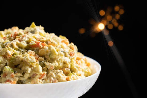 Olivier russian salad a classic recipe with mayonnaise an incredible taste on a black background with bokeh of sparklers for christmas and new year