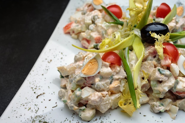 Olivier salad on a white plate on a dark background