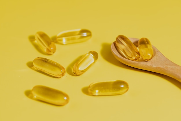 Omega-3 fish oil capsules in the wooden spoon on yellow background for healthcare concept