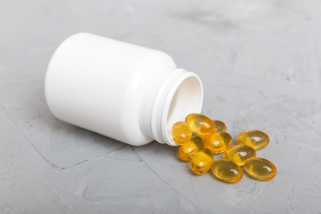 Omega3 capsules lie in white bottle on a table background Fish oil tablets top view Biologically active additives omega 6 omega 9 vitamin A E vitamin D vitamin D3 evening primrose oil