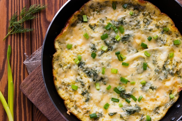 Omelet in a frying pan sprinkled with green onions