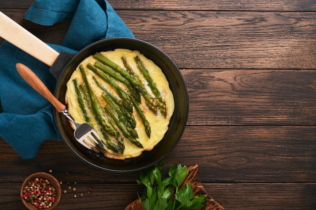 Omelet with asparagus Frittata or scrambled with asparagus in frying pan with parsley and pepper on old wooden table background Useful breakfast concept Top view