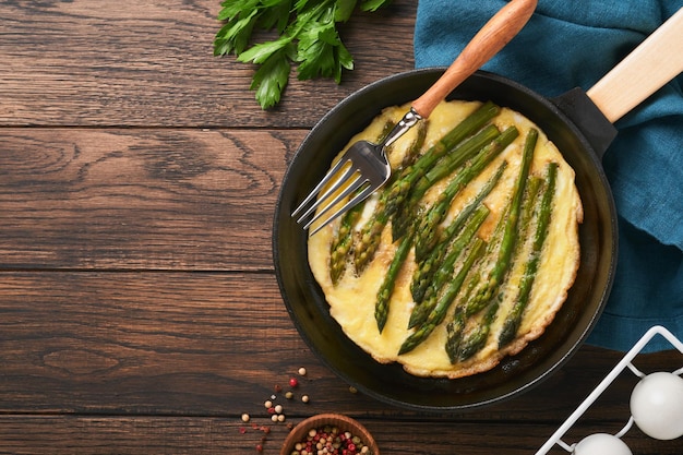 Omelet with asparagus Frittata or scrambled with asparagus in frying pan with parsley and pepper on old wooden table background Useful breakfast concept Top view