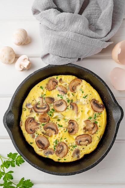 Omelette with mushrooms and herbs in a pan on a white wooden background Healthy breakfast