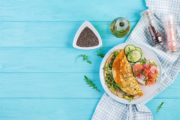 Omelette with radish, green arugula and sandwich with salmon on white plate