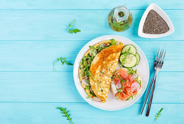 Omelette with radish, green arugula and sandwich with salmon on white plate