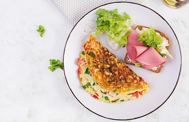 Omelette with tomatoes cheese green onion and sandwich with ham on white plate Frittata italian omelet Top view