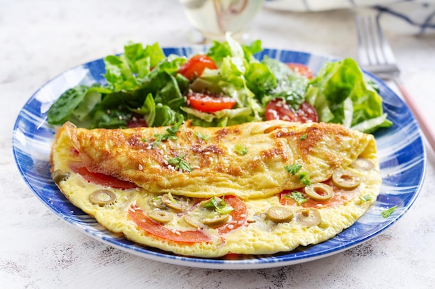 Omelette with tomatoes green olives and fresh salad on blue plate Frittata italian omelet