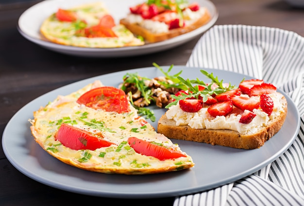 Omelette with tomatoes, ham and green onion on dark table